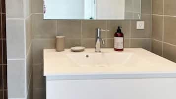 A bathroom with a white sink, a mirror, and a red bottle of soap.