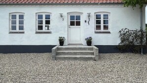 A white building with a red-tiled roof, a white door, and two potted plants on the front steps.
