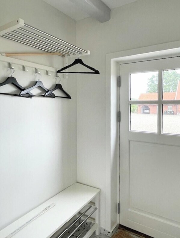 A room with a white door, a window with a view of buildings, and a clothes rack with hangers.
