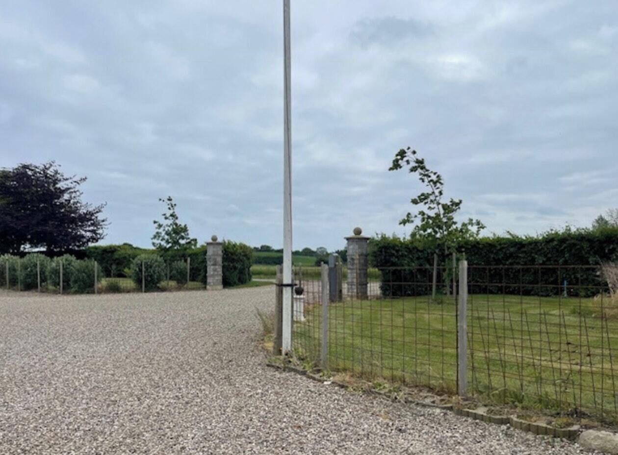 A gravel driveway leading to a fenced property with a tall pole and stone structures.