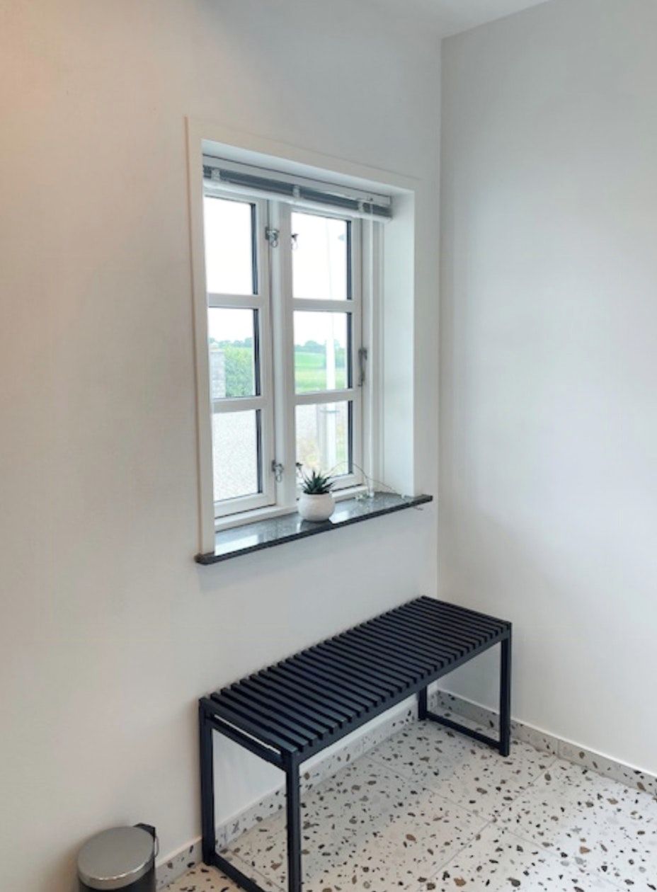 A room with a window, a bench, and a small trash bin.