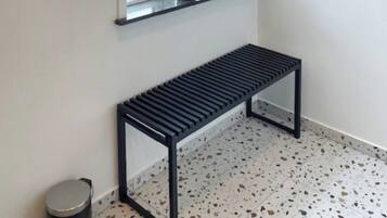 A room with a window, a bench, and a small trash bin.
