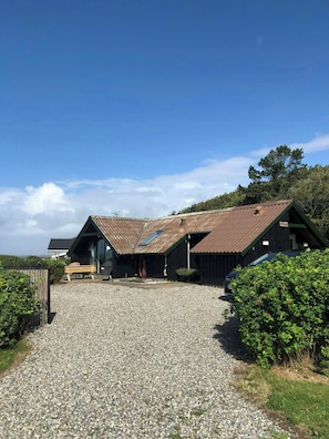A rustic building with a gravel driveway, a bench, and a car parked nearby. - Holiday home with sea views over the Western Sea (Vestervig)