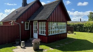 Ein rotes Holzhaus mit geneigtem Dach, einer Veranda und einem großen Fenster.