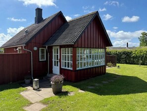 Ein rotes Holzhaus mit geneigtem Dach, einer Veranda und einem großen Fenster.