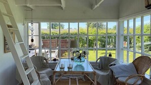 Ein sonnendurchfluteter Raum mit Tisch, Stühlen und Blick auf Grün.