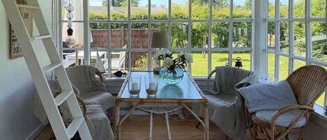 Une pièce baignée de lumière, avec une table, des chaises et une vue sur la verdure à l’extérieur.