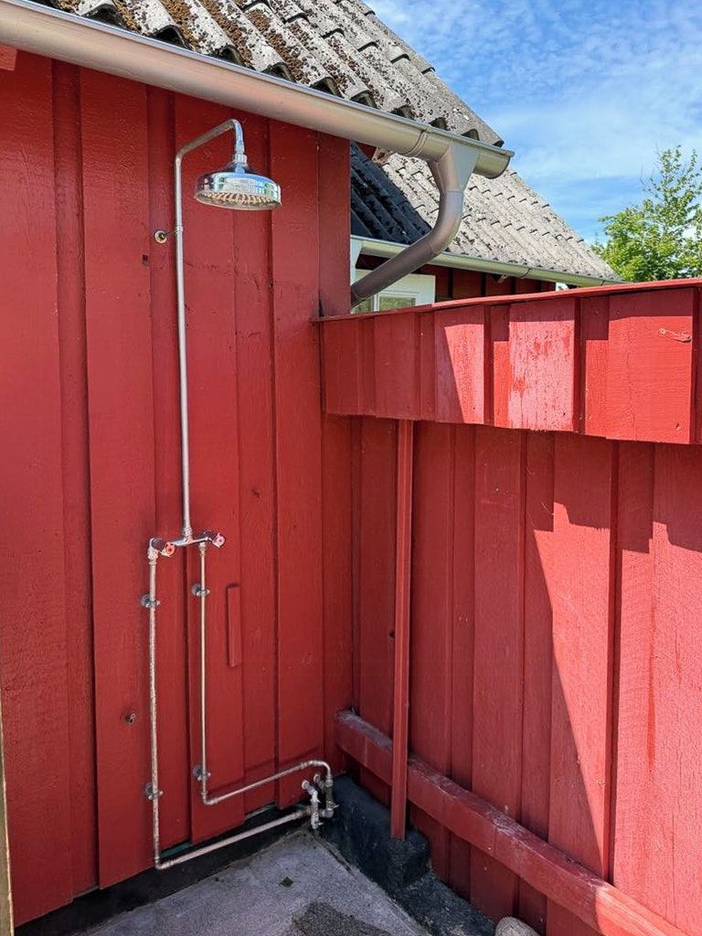 Una estructura roja de madera con cabezal de ducha y tuberías, presumiblemente un baño o cuarto de servicio.