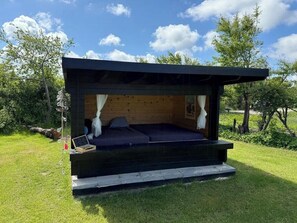 Ein moderner Schlafbereich im Freien mit Holzkonstruktion, einer Matratze und einem kleinen Tisch.