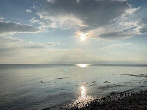 Ein Strand mit ruhigem Wasser, blauem Himmel und der Sonne, die sich auf der Oberfläche spiegelt.