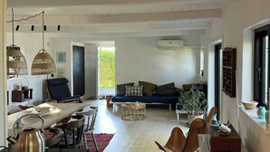 Uma sala de estar ampla com sofá, mesa de jantar, cadeiras e área de cozinha com chaleira.