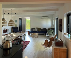 Ein geräumiger Wohnbereich mit einer Couch, einem Esstisch, Stühlen und einer Küchenzeile mit Wasserkocher.