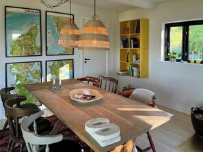 A dining area with a wooden table, wicker pendant lights, a yellow bookshelf, and framed maps on the wall. - Holiday home with view of Dalby Bay (Mesinge)