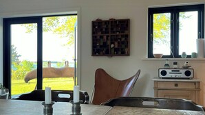 Uma sala de jantar com uma mesa de mármore, duas velas, uma luminária de vime no teto, um rádio e vista para cavalos e vegetação lá fora.