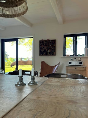 Ein Essbereich mit einem Marmortisch, zwei Kerzen, einer Weidenkorb-Deckenleuchte, einem Radio und Blick auf ein Pferd und Grünfläche draußen.