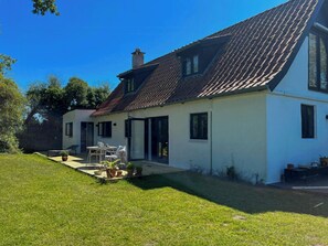 A two-story house with a tiled roof, a patio with a table and chairs, and a lawn. - Holiday home with view of Dalby Bay (Mesinge)
