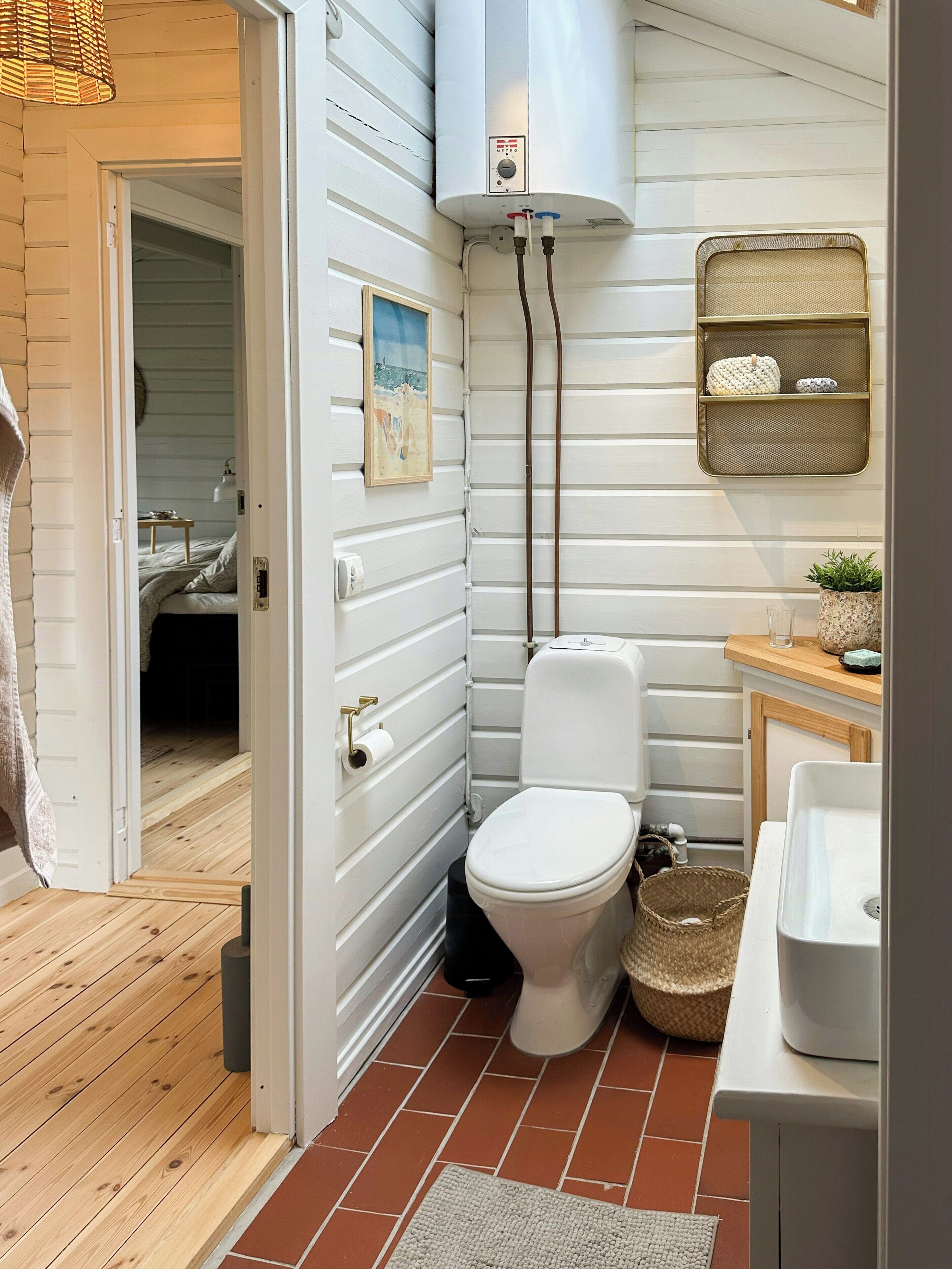 A compact bathroom with a toilet, a sink, a shower area, and a small shelf with toiletries.