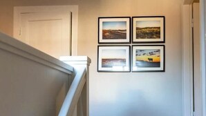 A hallway with a white door, a staircase, and four framed pictures on the wall. - Brick house in secluded setting (Wingst)