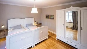 A bedroom with a bed, bedside table, lamp, wardrobe, and a window. - Brick house in secluded setting (Wingst)