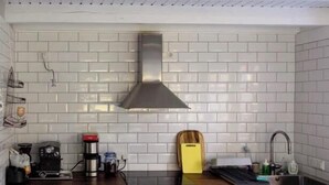 A kitchen with white subway tiles, a stainless steel range hood, a coffee maker, a yellow cutting board, and a built-in oven. - Brick house in secluded setting (Wingst)