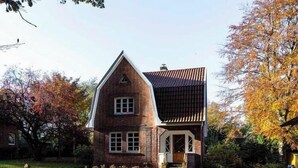 A brick house with a gabled roof, a front porch, and a small front yard. - Brick house in secluded setting (Wingst)