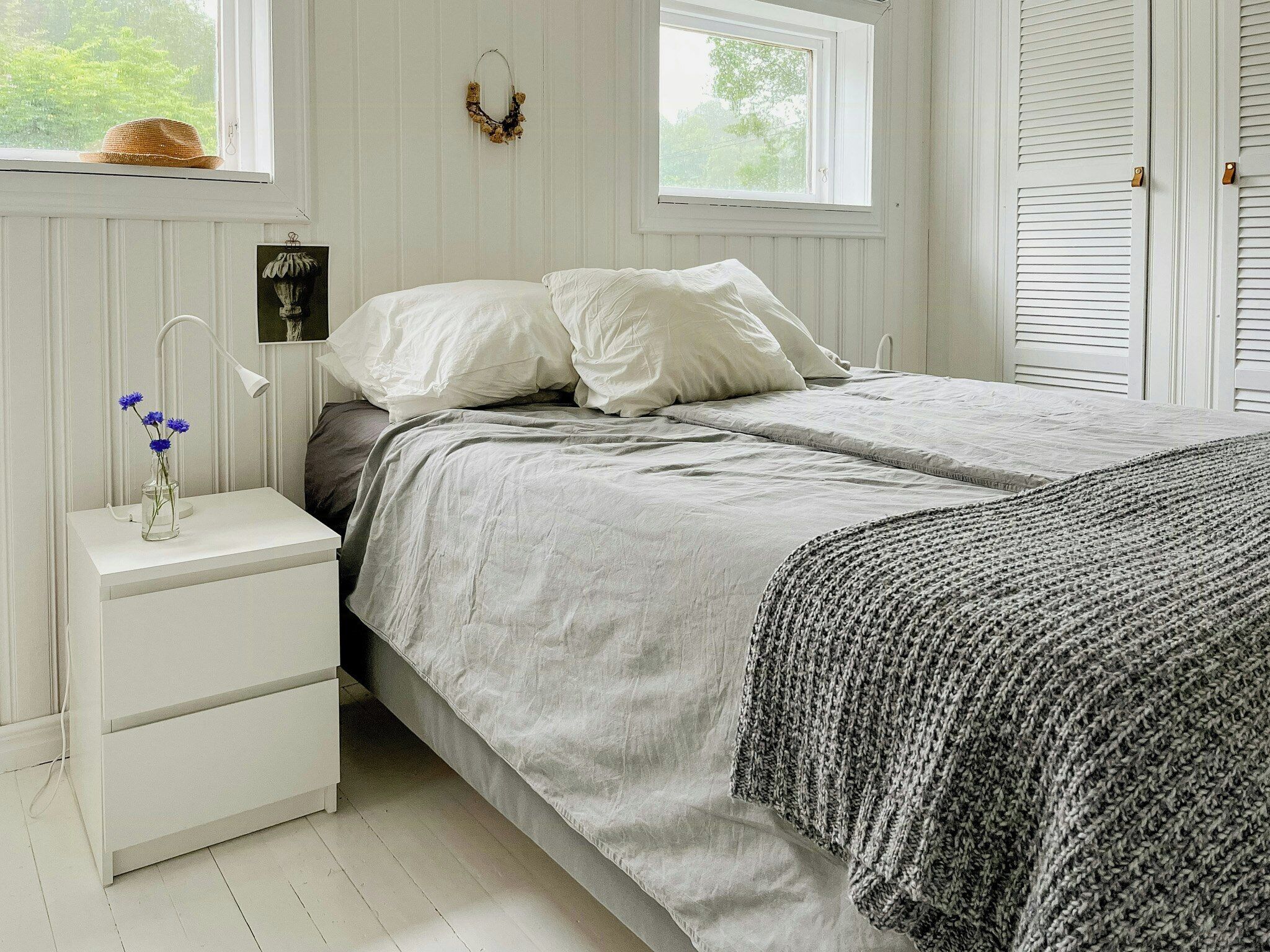 A bedroom with a bed, bedside table, lamp, and a window with a view of greenery.