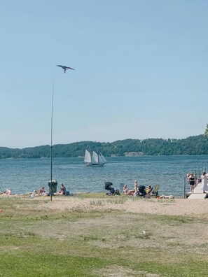 A lakeside view with a sailboat, people relaxing on the shore, and a kite flying. - Cozy cabin with fjord view and fireplace (Uddevalla)