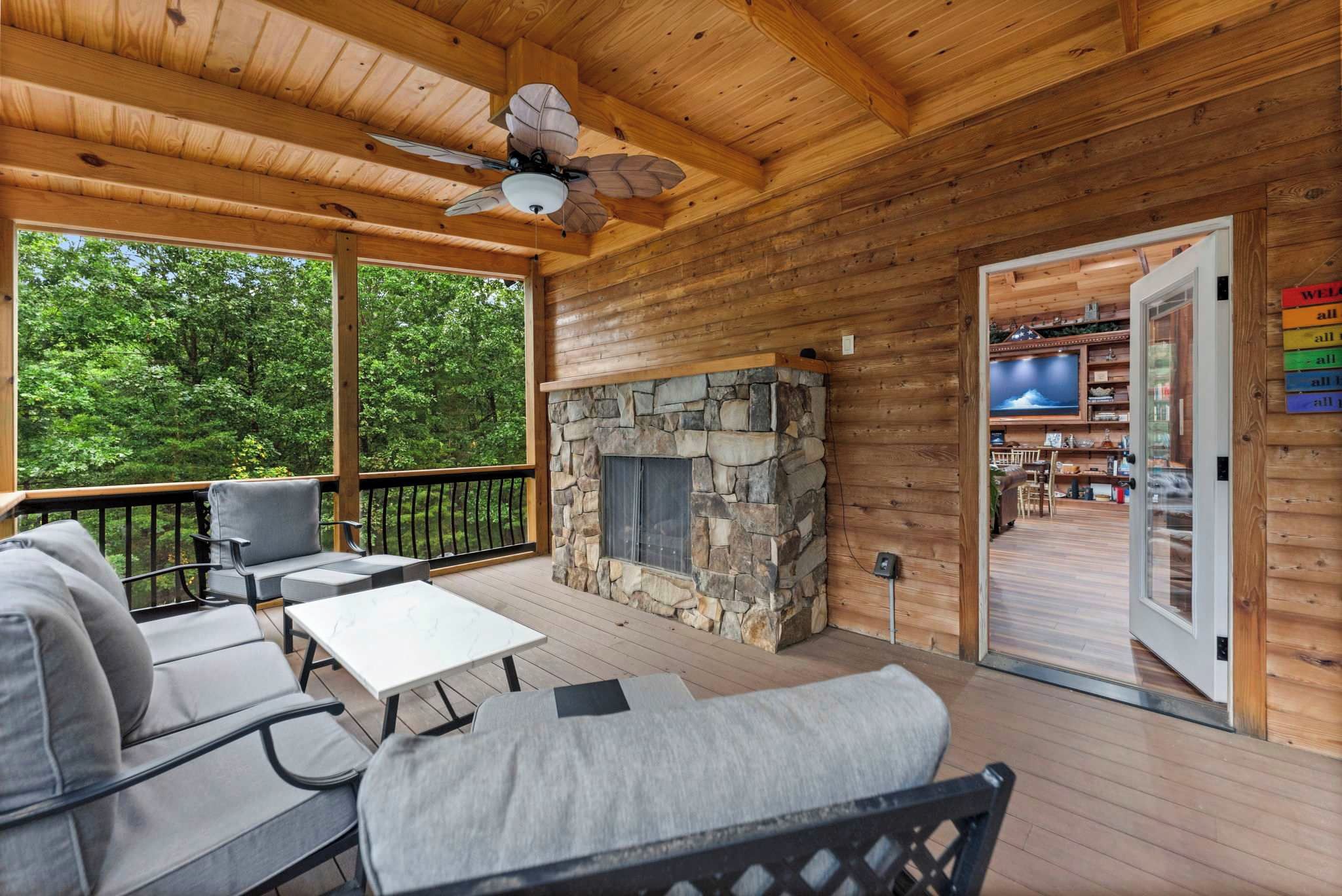 A wooden deck with a stone fireplace, outdoor seating, and a television in the background.