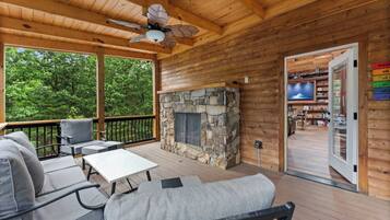 A wooden deck with a stone fireplace, outdoor seating, and a television in the background.