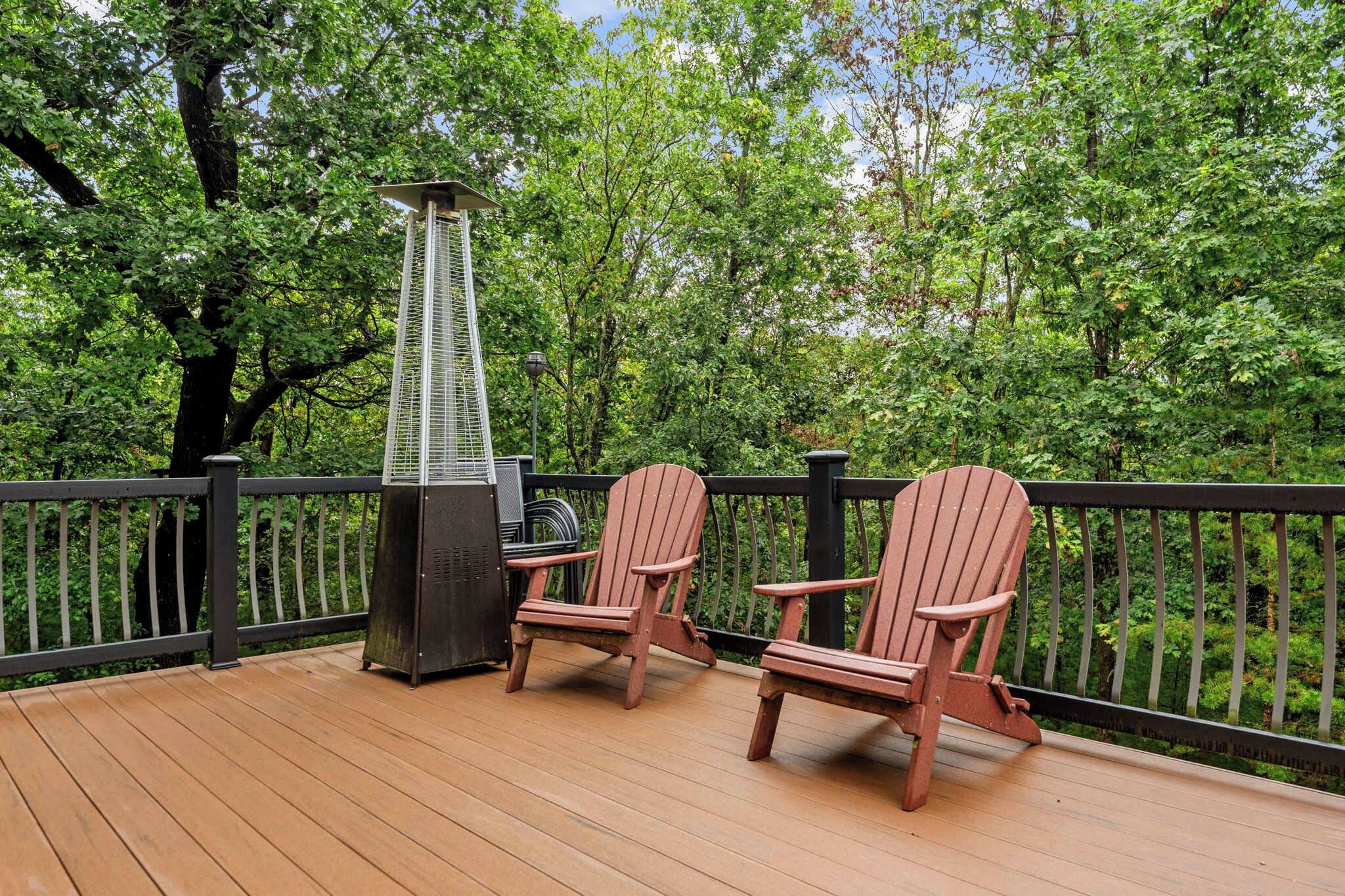 Eine Terrasse mit Grill, zwei Adirondack-Stühlen und einem Geländer.