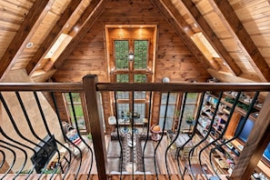 Interior de madera con techos altos, un área de estar central, una escalera y vistas al exterior.