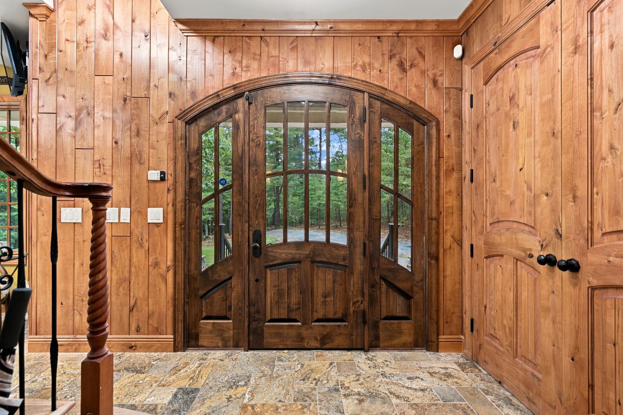A wooden door with a glass panel, a stone-tiled floor, and a wooden staircase.