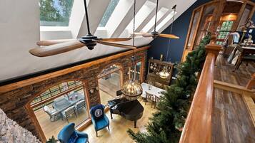 A spacious loft with a high ceiling, exposed wooden beams, a piano, and a dining area with a view of the outdoors.