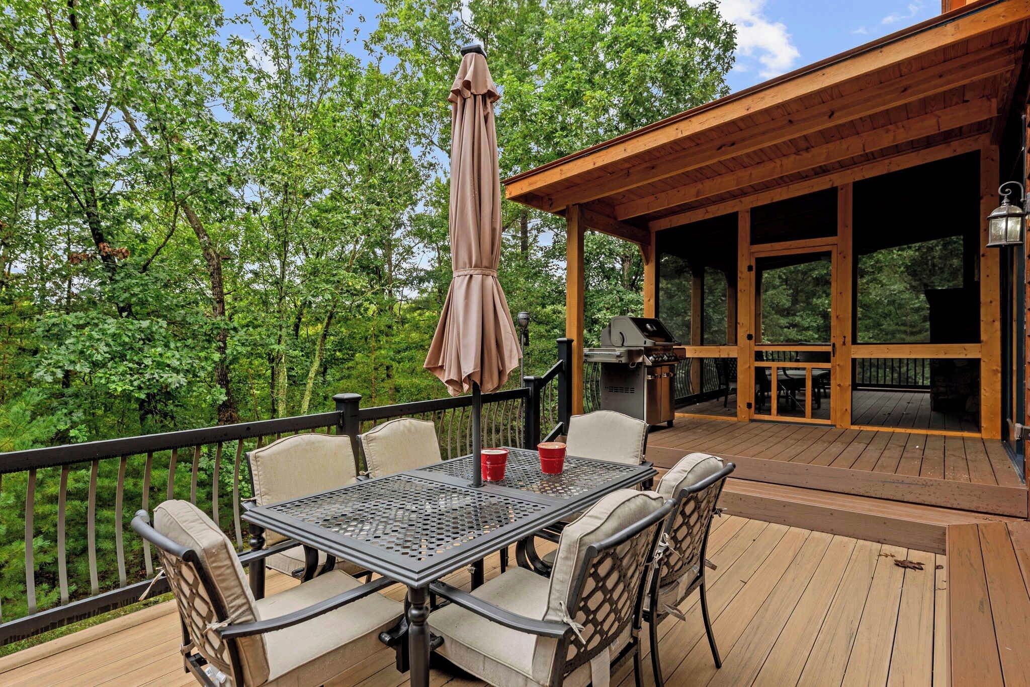 Terraza exterior con mesa y sillas, una parrilla y una zona cubierta con vistas a árboles.