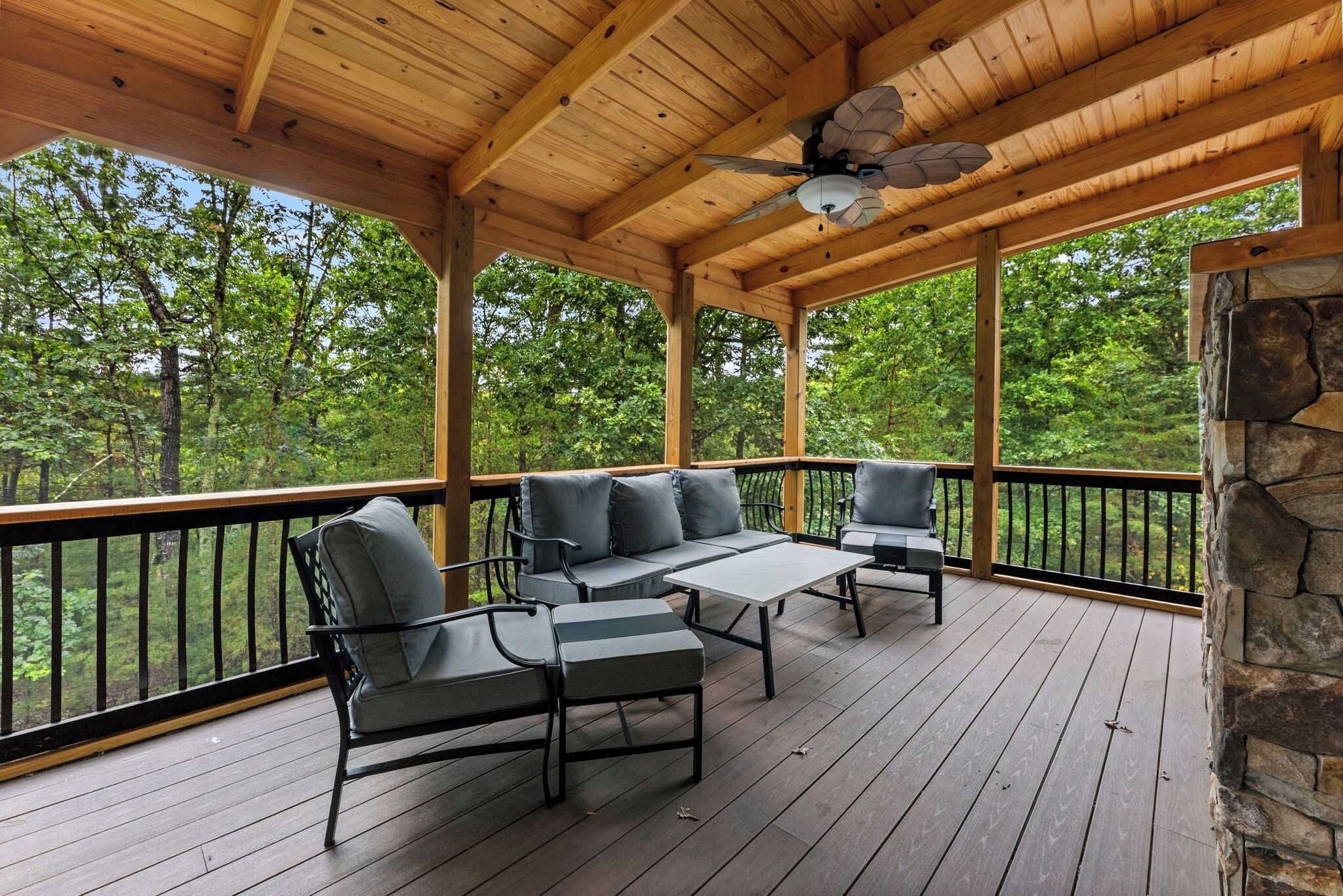 A covered outdoor deck with a wooden ceiling, a stone wall, and a view of a forest.