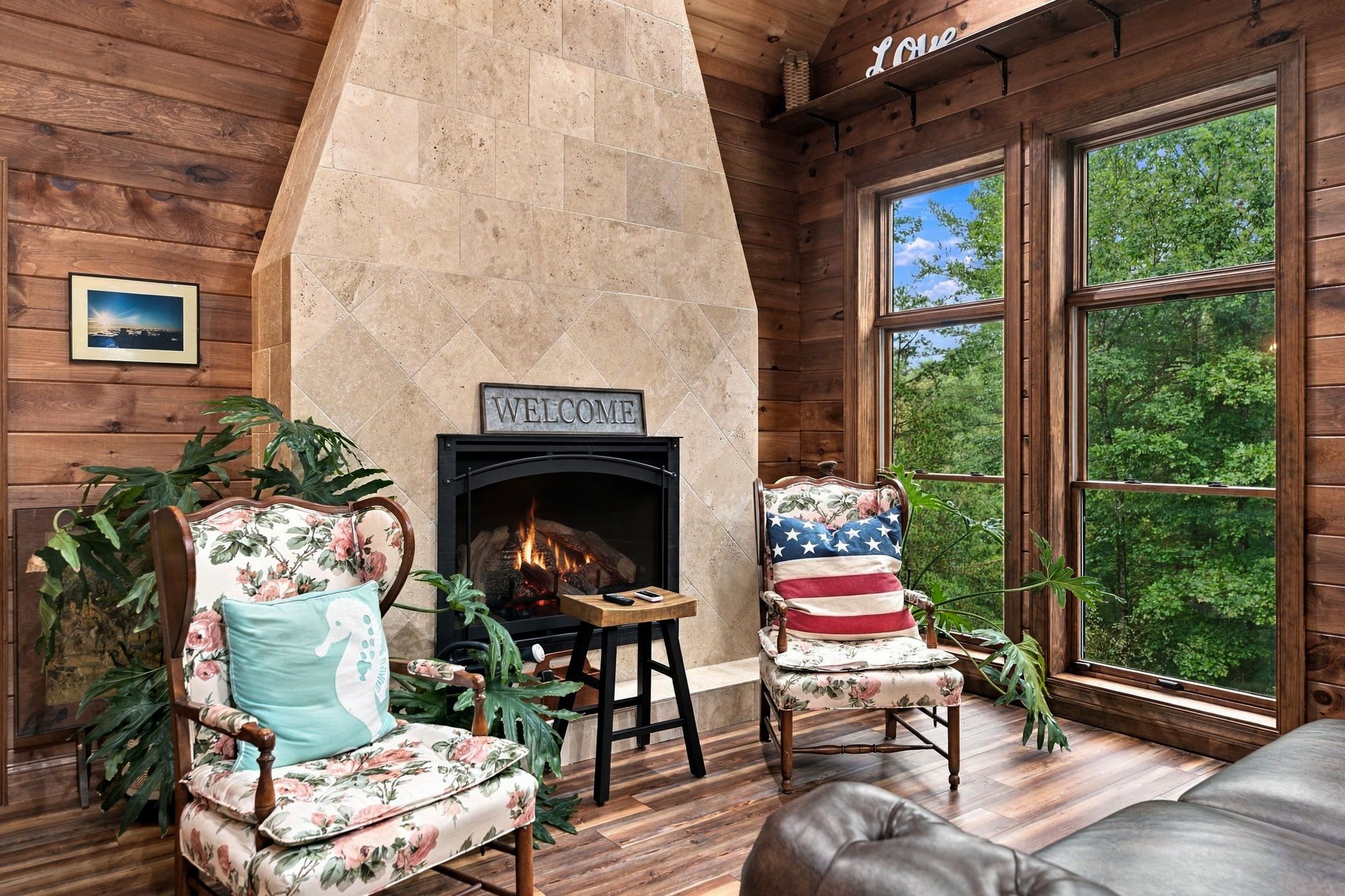A cozy room with a fireplace, wooden walls, and a large window offering a view of trees.