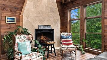 A cozy room with a fireplace, wooden walls, and a large window offering a view of trees.