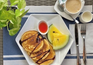 Un desayuno con tortitas, fruta y bebidas sobre una mesa.