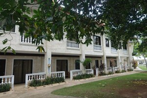 A multi-story building with balconies, a paved walkway, and greenery.