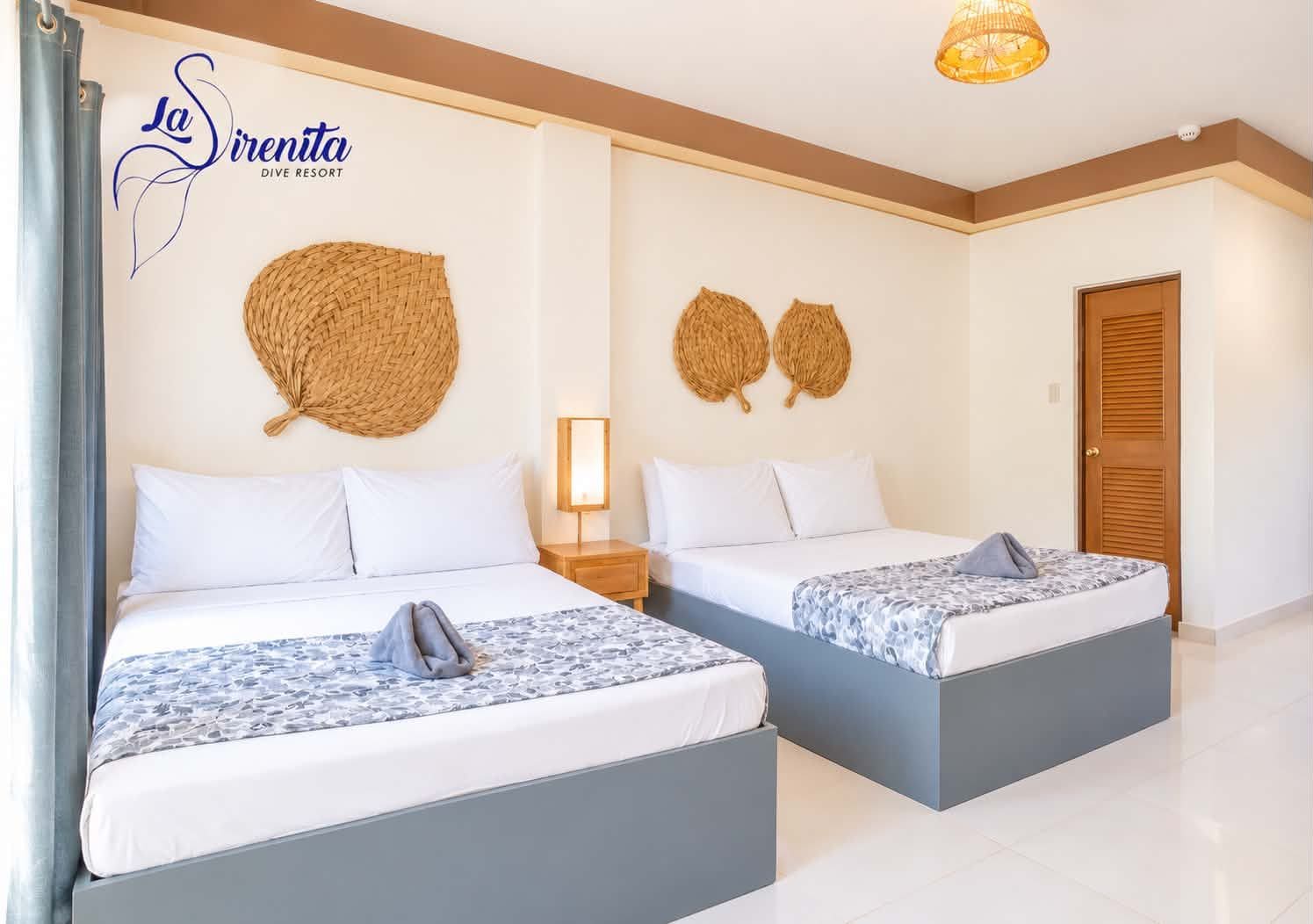 A hotel room with two beds, a woven wall decoration, a bedside lamp, and a wooden door.