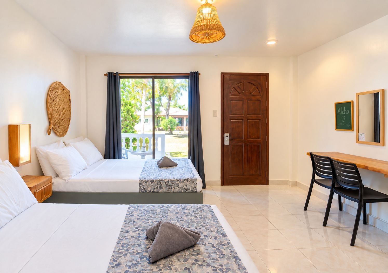 A hotel room with a bed, a desk, and a chair. There is a window with curtains, a door, and a wall-mounted light fixture.