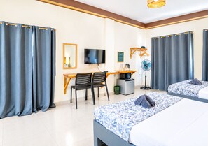 A hotel room with a bed, a desk with chairs, a television, and a fan. - La Sirenita Dive Resort (Panglao)
