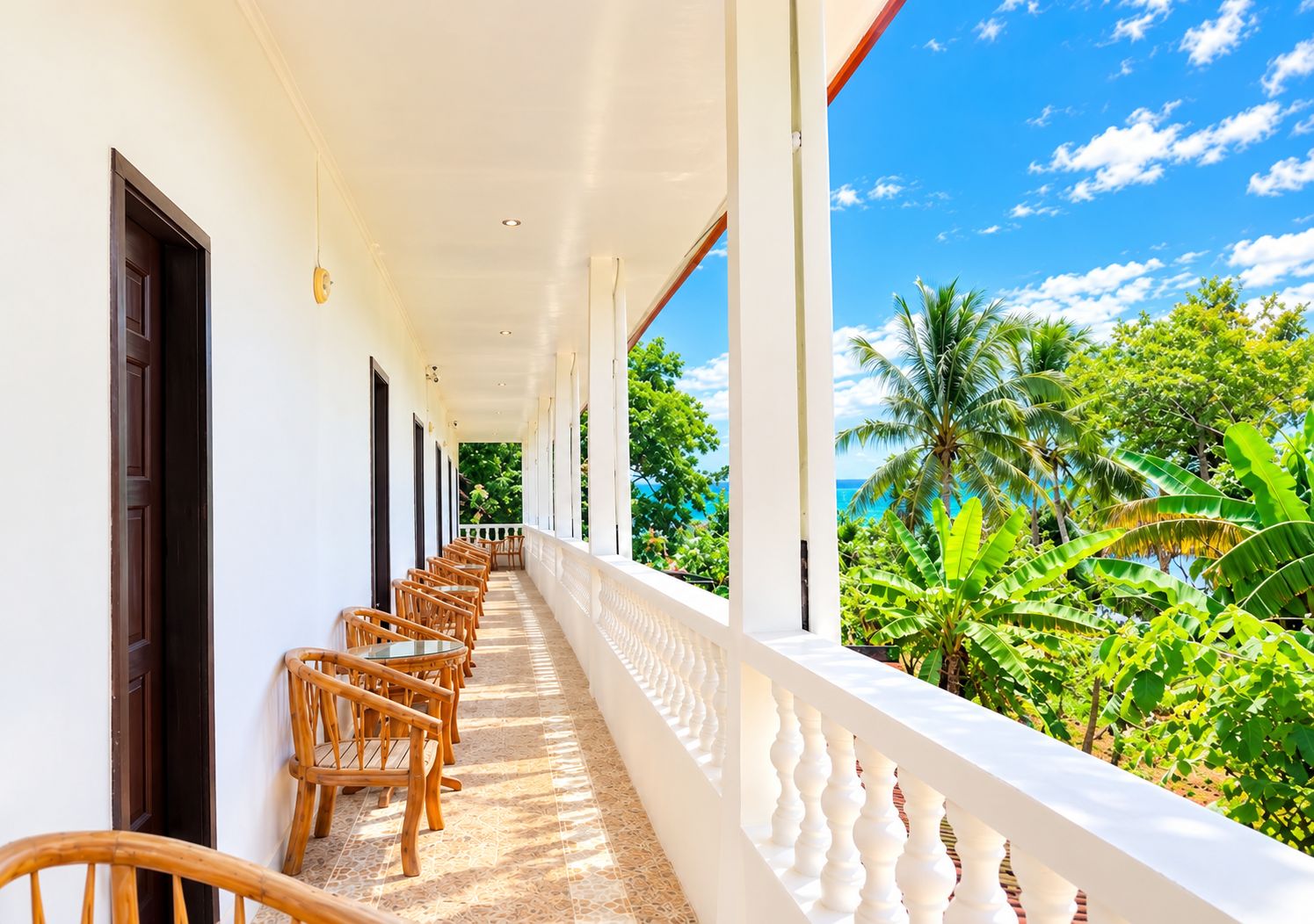 A covered corridor with rows of wicker chairs and a view of lush greenery and a clear blue sky.