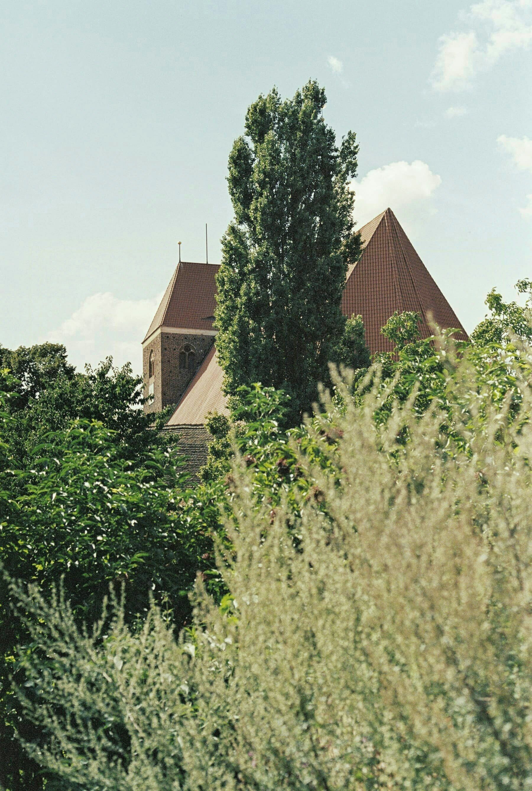 A building with a triangular roof and a visible tower, surrounded by greenery.
