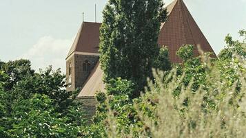 A building with a triangular roof and a visible tower, surrounded by greenery.
