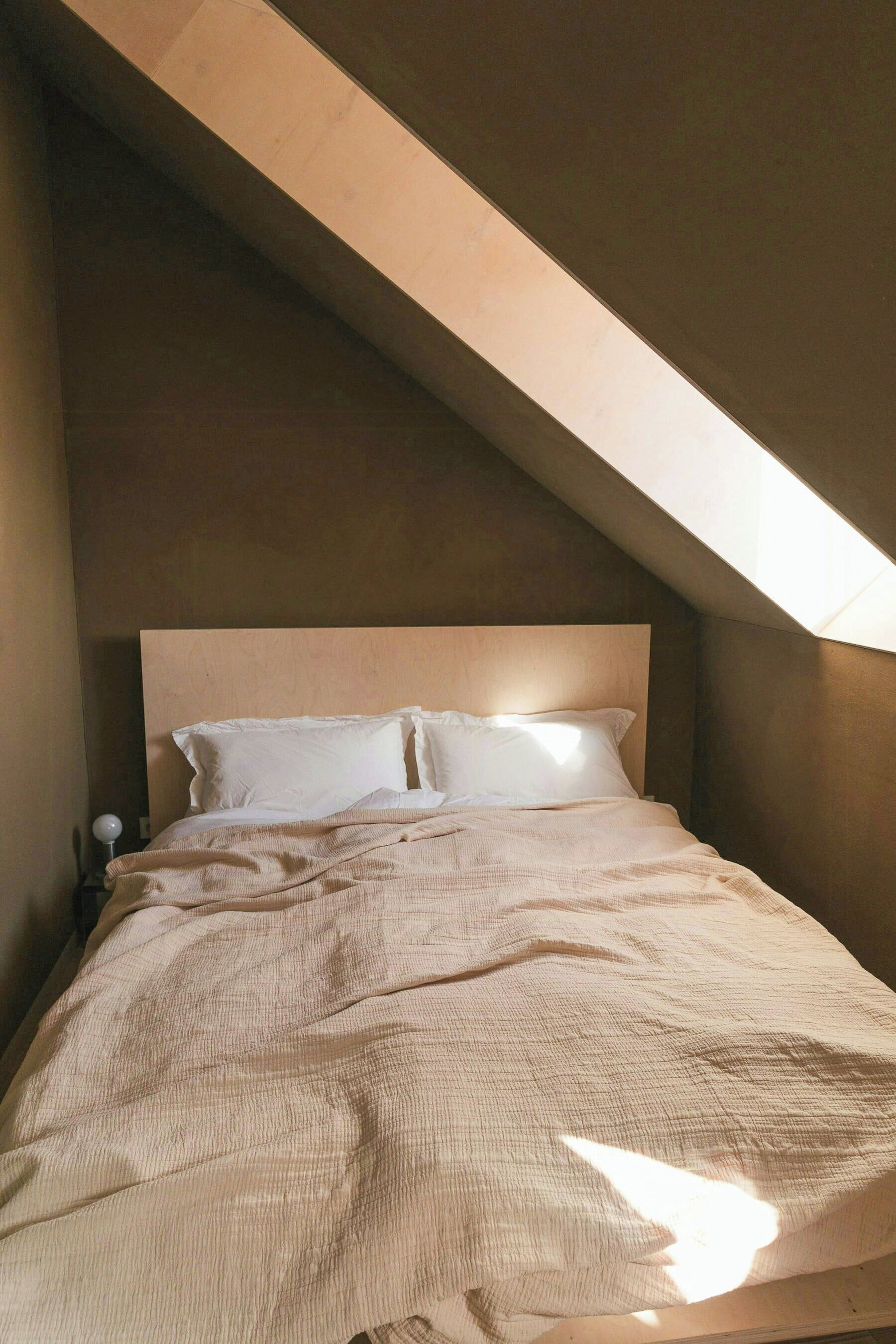 Une chambre avec un plafond en pente, un lit avec une literie blanche et une table de chevet avec une lampe.