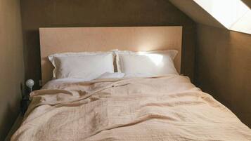 Une chambre avec un plafond en pente, un lit avec une literie blanche et une table de chevet avec une lampe.