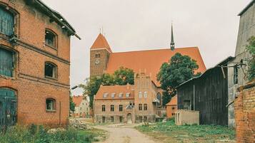 A historical building with a clock tower, a church, and a dirt path leading to the entrance.