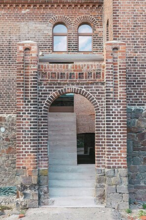 A brick building with a central arched doorway, two windows above, and a stone base. - Attic flat with balcony and sauna in Naulitz (Werben)