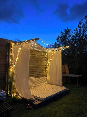 A cozy outdoor seating area with a mattress, draped fabric, and string lights. - House with soul in Klitmøller (Klitmøller)